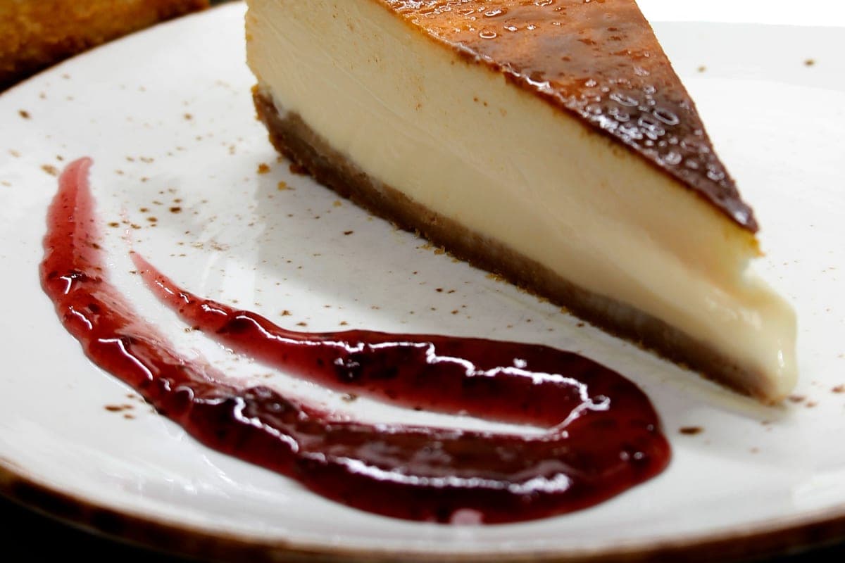 A slice of Spanish Basque burnt cheesecake with a dark caramelized top and creamy pale center, served on a white plate with a swirl of berry sauce