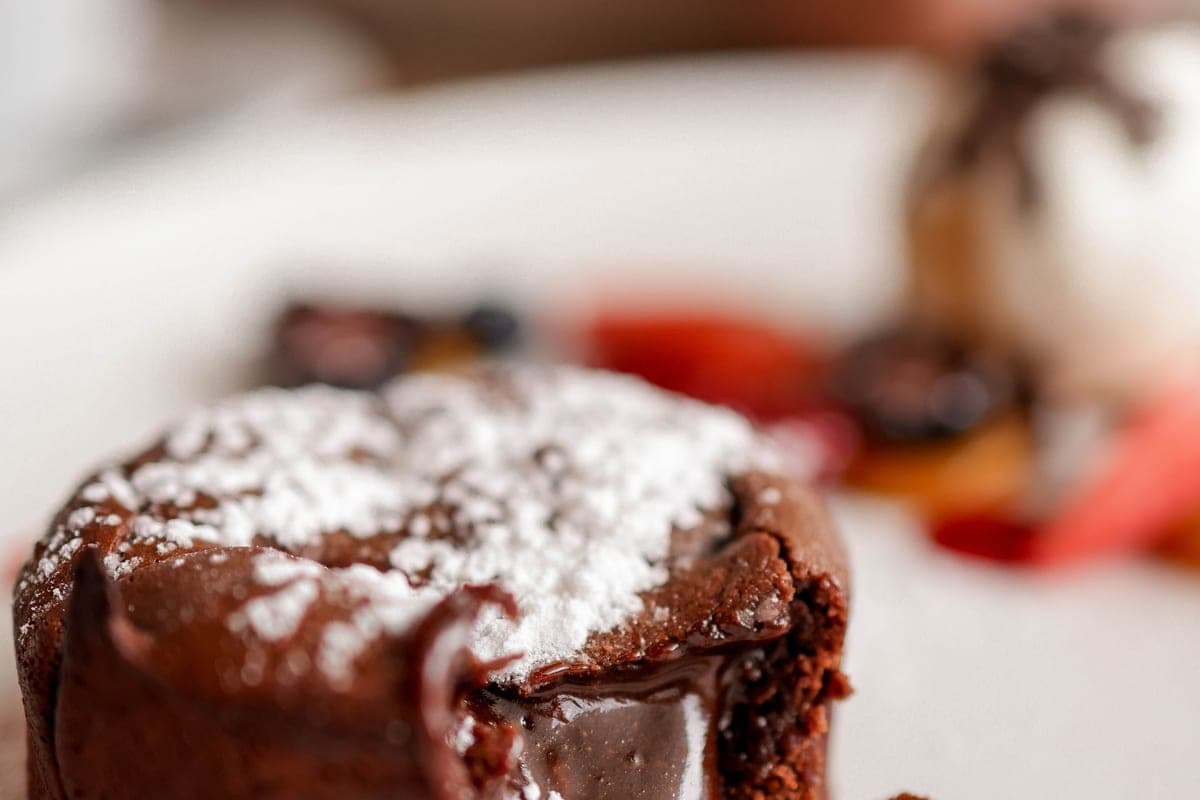 A chocolate molten lava cake dusted with powdered sugar, cut open with warm chocolate flowing from the center, served with berries