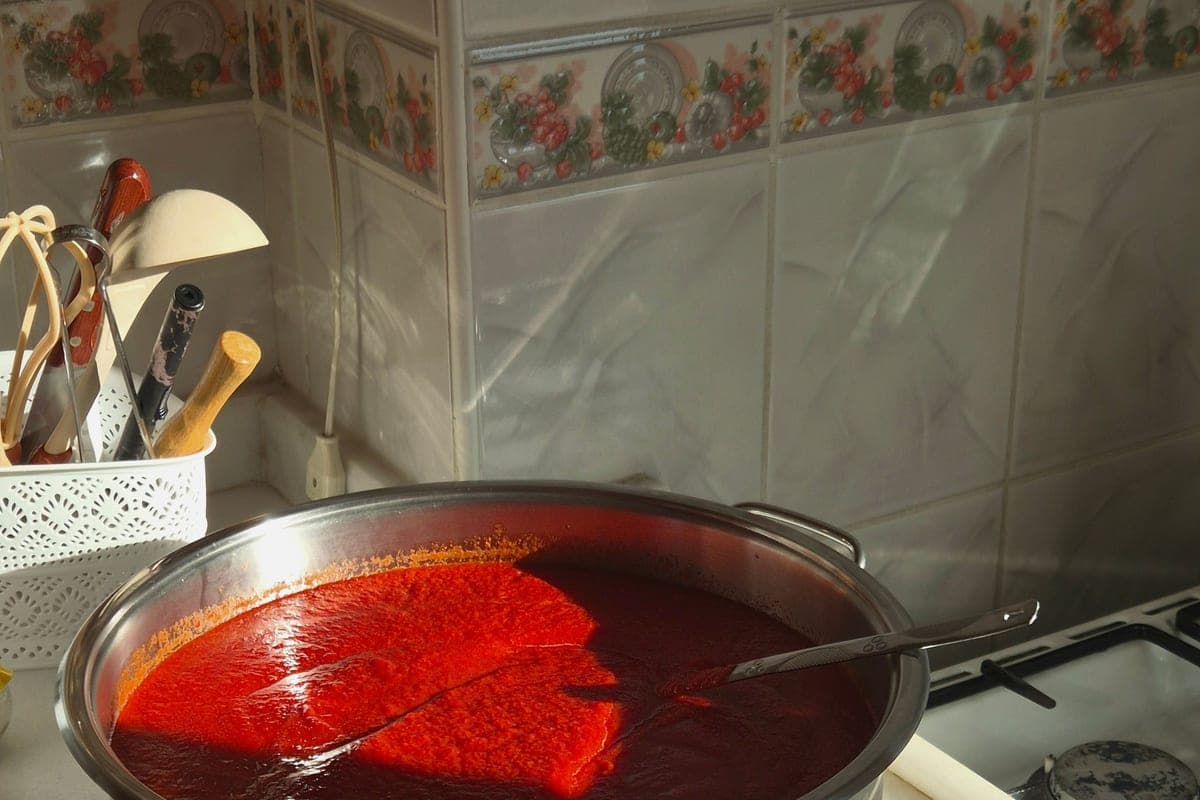 A wide pot of bright red homemade Italian tomato sauce simmering on the stove in a home kitchen
