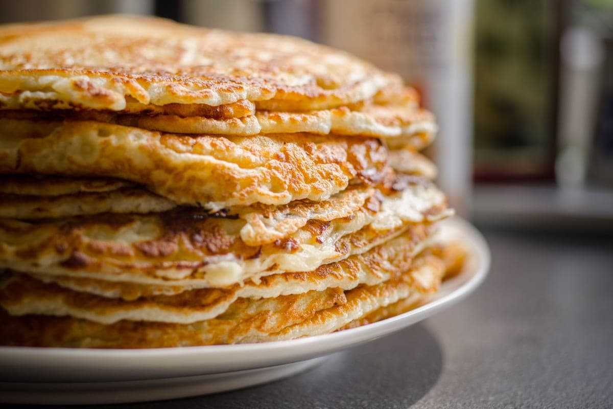 A tall stack of fluffy golden buttermilk pancakes on a white plate