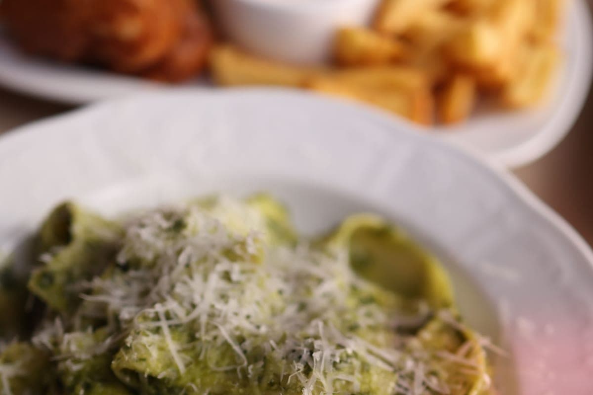 A plate of pasta tossed in bright green homemade basil pesto and topped with grated Parmesan cheese