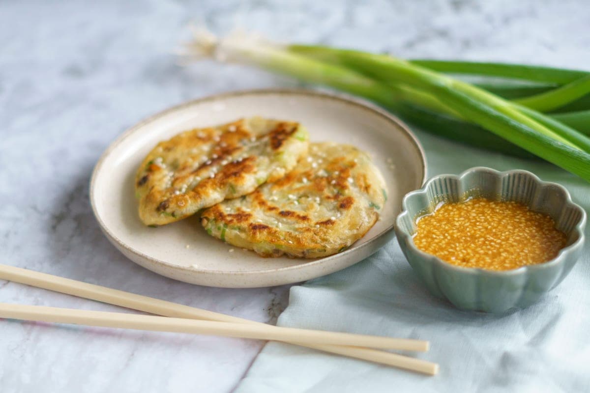 Golden crispy scallion pancakes on a plate with fresh green onions, a small dish of dipping sauce and chopsticks