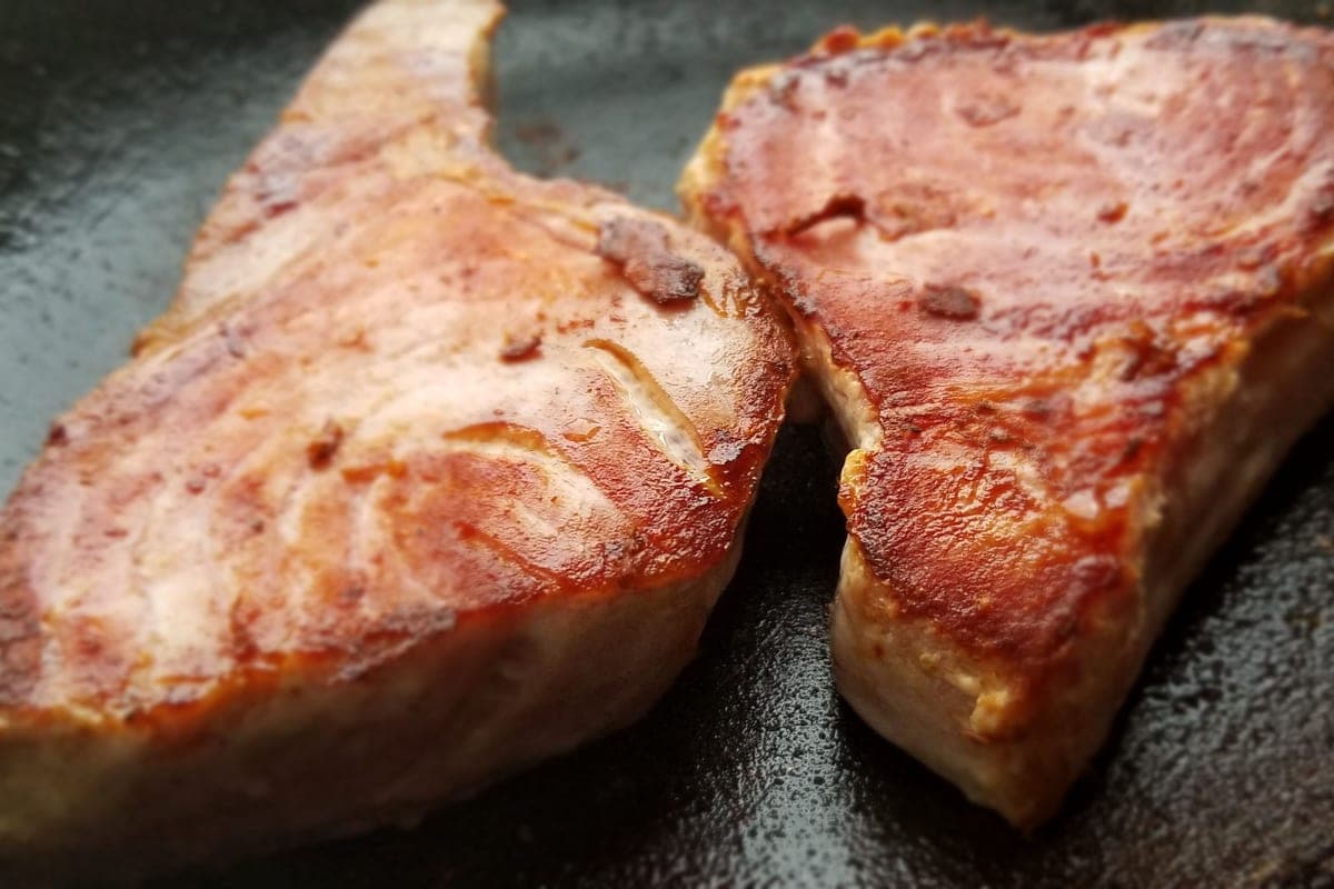 Two thick swordfish steaks with a golden-brown sear cooking in a hot cast-iron skillet