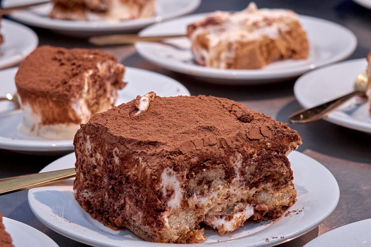 A generous square of classic Italian tiramisu with layers of espresso-soaked ladyfingers and mascarpone cream, dusted with cocoa powder