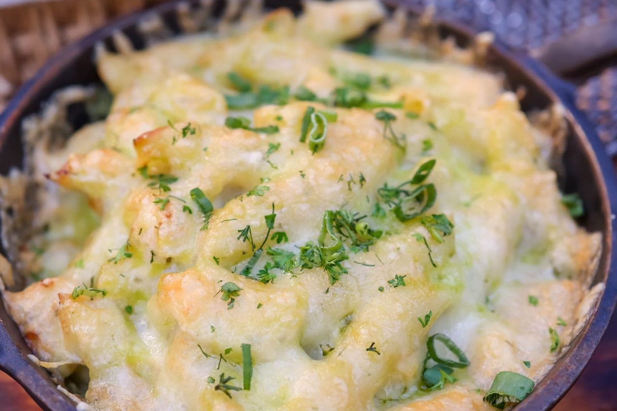 Baked macaroni and cheese with a bubbling, lightly browned cheese top and fresh herbs, in a dark baking dish
