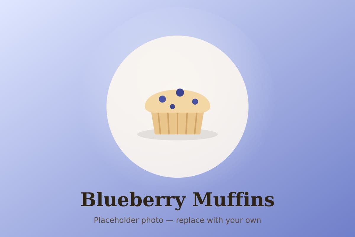 Tall bakery-style blueberry muffins with golden streusel tops in a muffin tin, one split to show the berries inside
