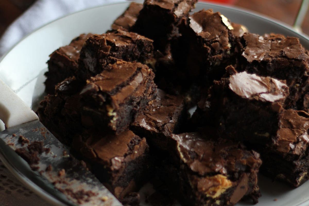 A plate piled with squares of dark, fudgy chocolate brownies with shiny crackly tops