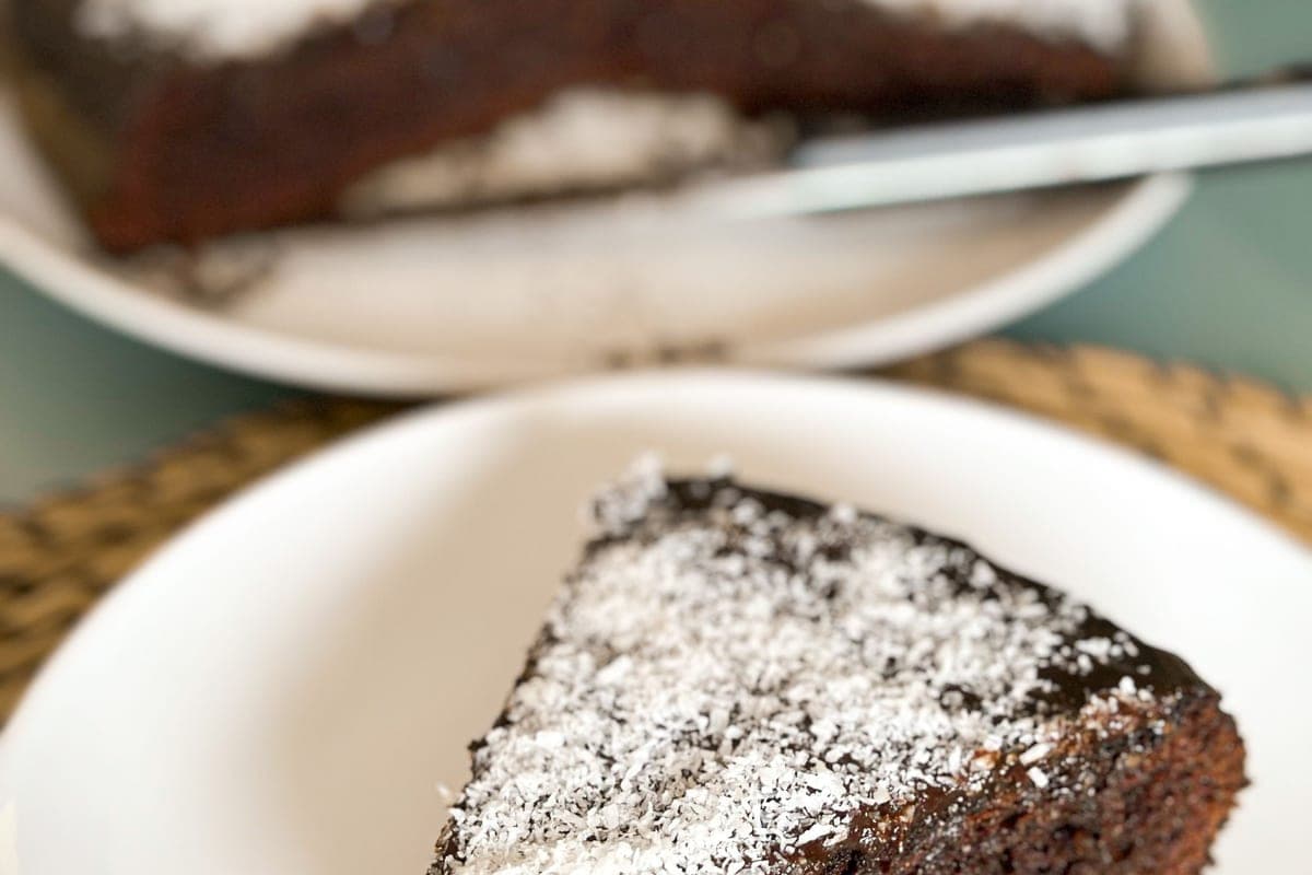 A slice of moist dark chocolate cake dusted with powdered sugar on a white plate