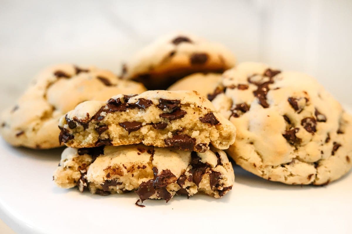 A stack of thick chocolate chip cookies, one broken open to show a soft center with melted chocolate chunks