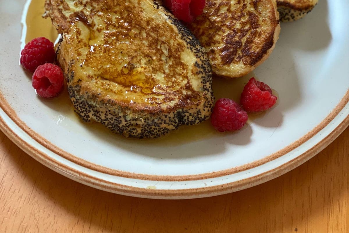 Thick slices of golden French toast with fresh raspberries and syrup on a white plate