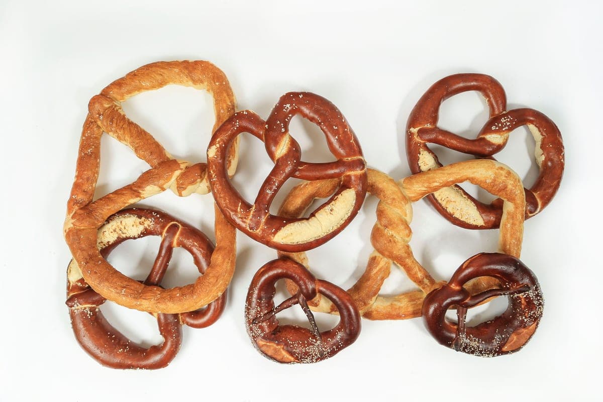 A row of homemade German pretzels with deep brown crusts and pale split bellies laid out on a white surface