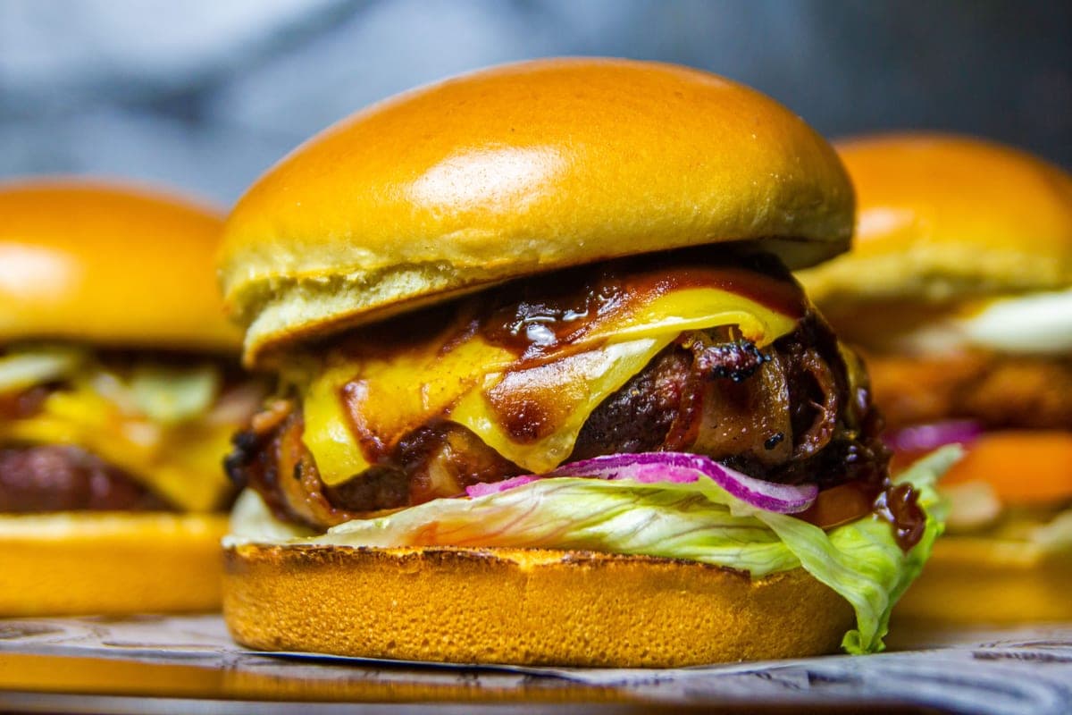 A loaded cheeseburger on a glossy toasted brioche bun with melted cheddar, a seared beef patty, lettuce and red onion