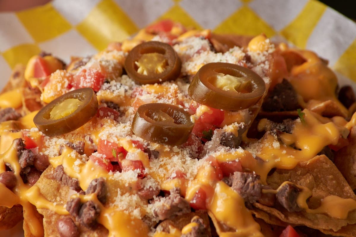 Loaded beef nachos covered in melted cheese sauce, diced tomatoes, grated cheese and sliced pickled jalapeños