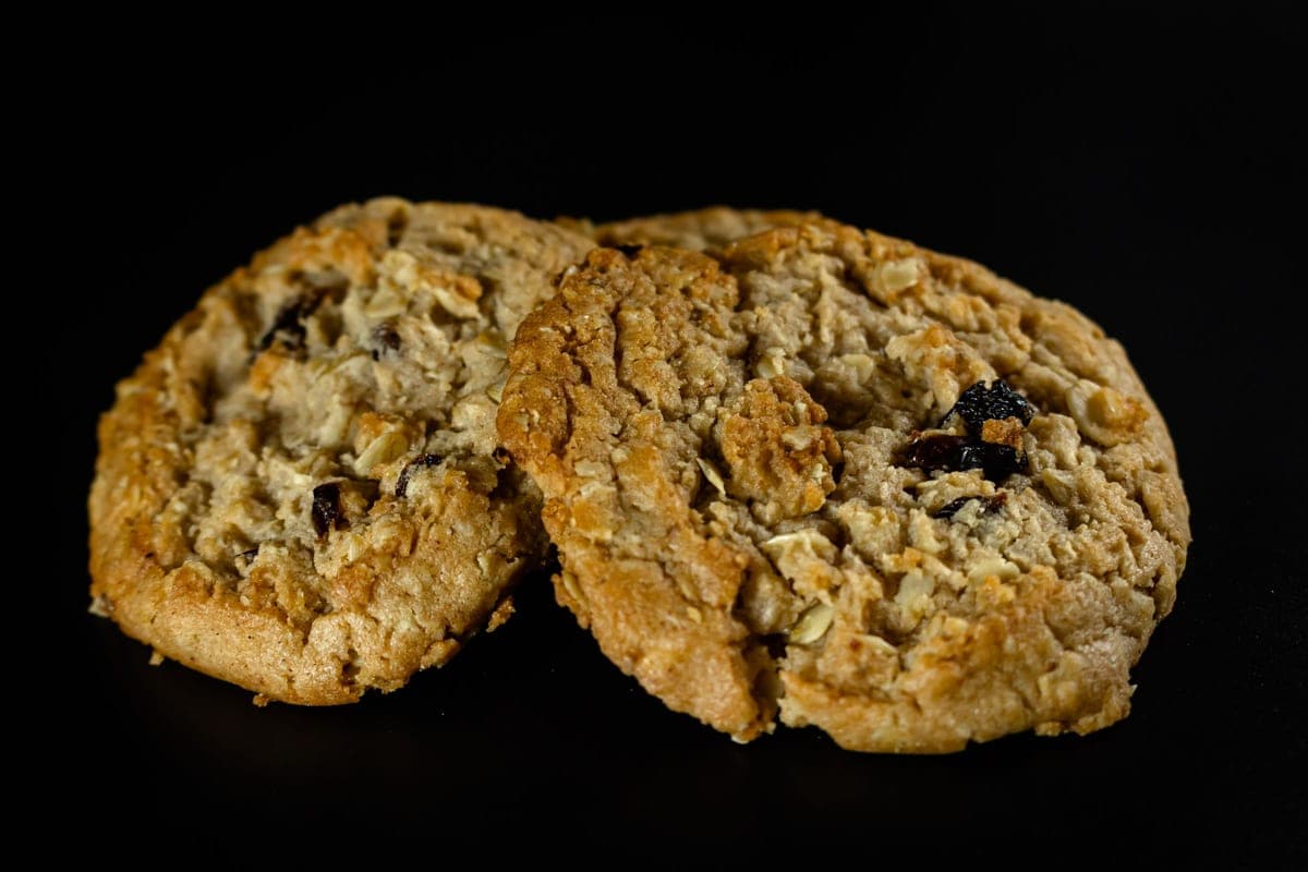 Two golden oatmeal raisin cookies side by side on a black background