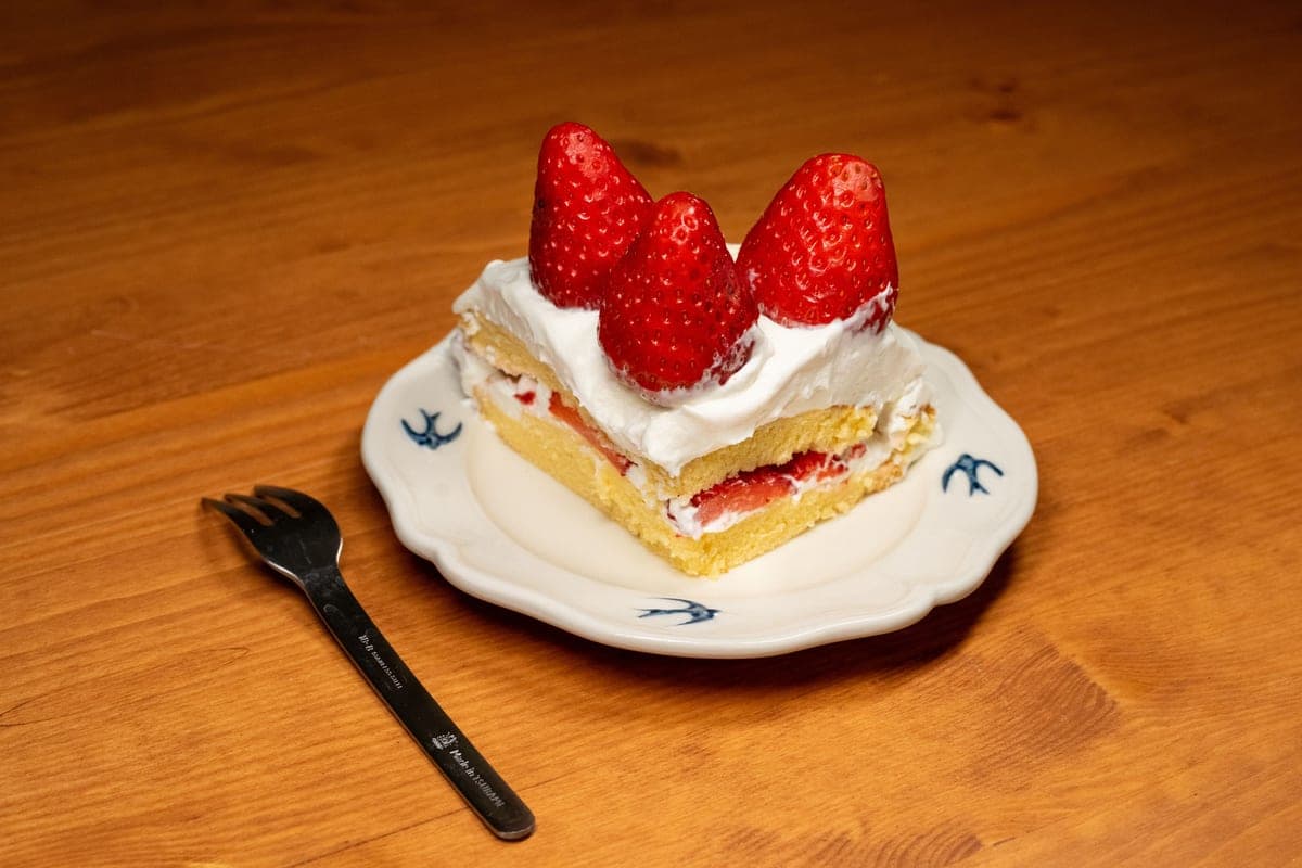 A slice of layered strawberry shortcake with fluffy sponge cake, whipped cream and fresh whole strawberries on a white plate